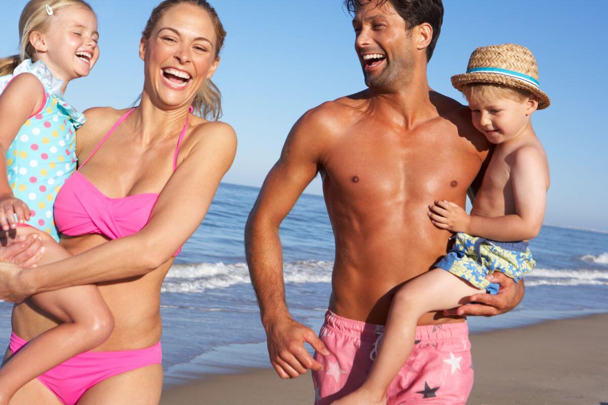 Happy family on summer holiday walking by the sea with young children