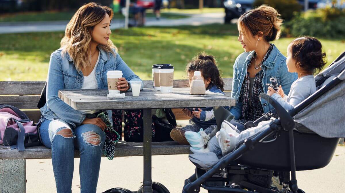 Two mothers talking over coffee while their children play