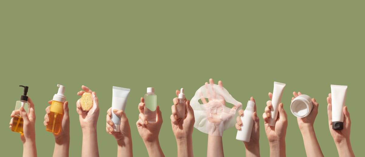 Hands holding a variety of Korean skincare products including oils, foams, toners, masks, and creams