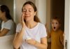 Skincare Minimalism, Korean Style: Fewer Steps, Lower Cost, Better Skin Mum applying moisturiser in the bathroom while her child interrupts, showing the reality of fitting skincare into busy family life