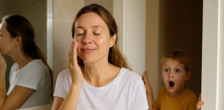 Mum applying moisturiser in the bathroom while her child interrupts, showing the reality of fitting skincare into busy family life